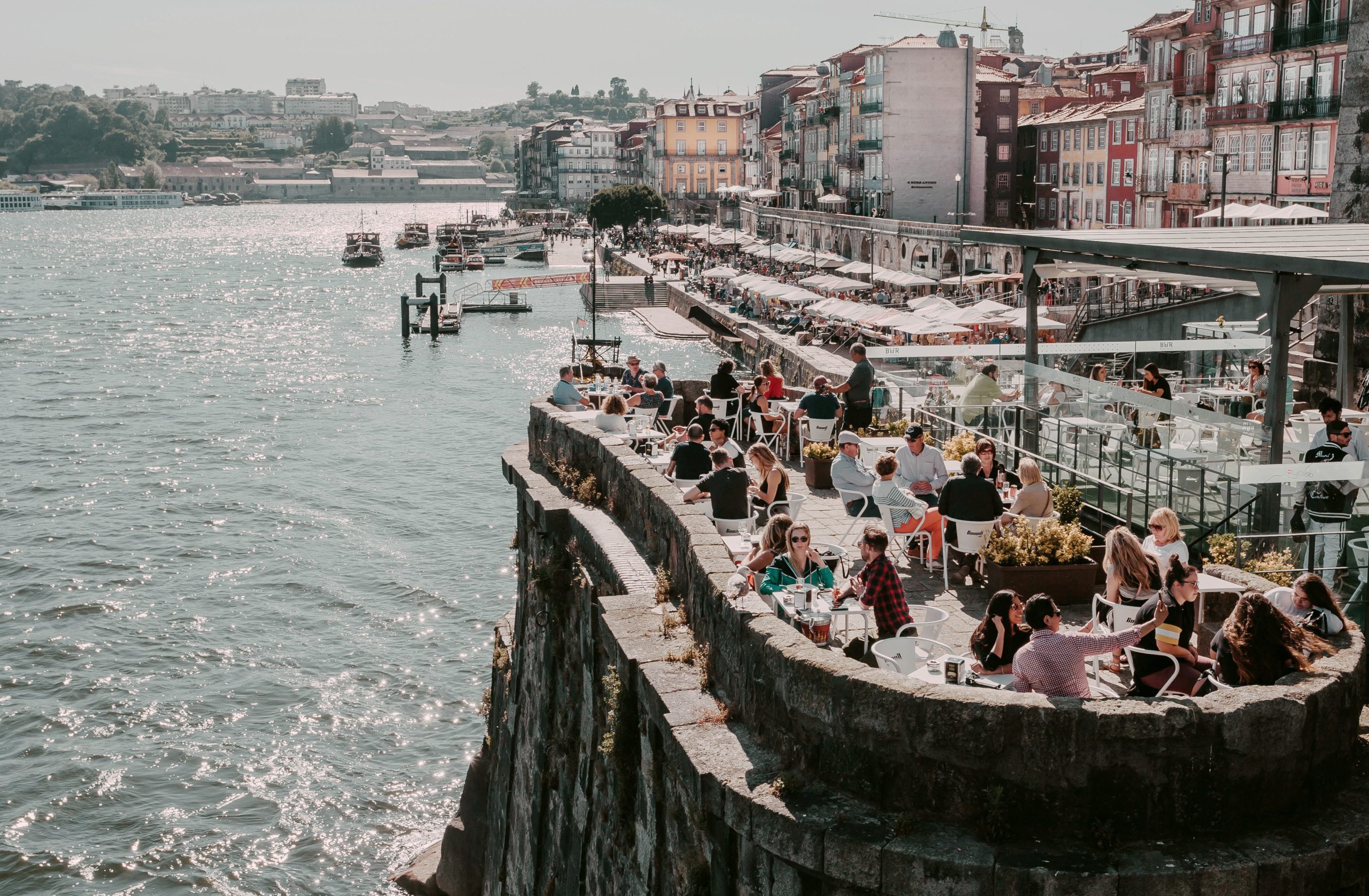 Old city houses over Douro river and many tourists having lunch at outdoor restaurant Porto, Portugal: Old city houses over Douro river and many tourists having lunch at outdoor restaurant on 21 May, 2019. Portuguese language has 250 million total speakers